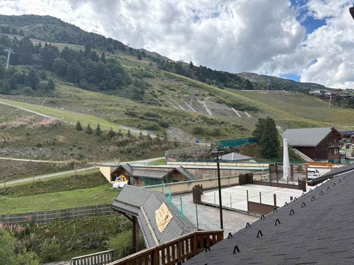 A view of a mountainous area with a building that has a sloped roof and a fenced area with a pathway leading to it.