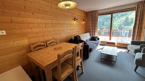 Una habitación acogedora con pared de madera, una mesa de comedor con sillas, un sofá, una mesita de centro y un ventanal con cortinas.