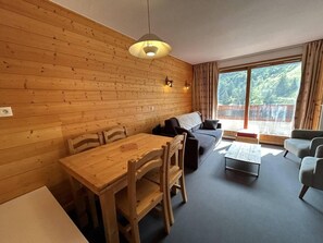 Una habitación acogedora con pared de madera, una mesa de comedor con sillas, un sofá, una mesita de centro y un ventanal con cortinas.
