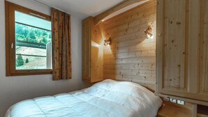 Un dormitorio con cabecera de madera, una ventana grande con cortinas y una cama con edredón blanco.