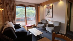 Una habitación acogedora con techo de madera, un sofá, dos sillones, una mesita y una ventana con vistas al verdor.
