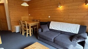 Una habitación acogedora con una pared de madera, un sofá gris, una mesa de comedor de madera con sillas y una pequeña mesa de centro de madera.
