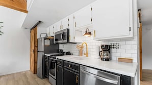 Een moderne keuken met witte kasten, roestvrijstalen apparatuur en een houten plafond.