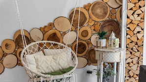 Een kamer met een hangstoel van macramé, een klein wit bijzettafeltje met een plant en een wand versierd met houten boomstammen.