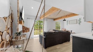 Een ruime woonkamer met een donkere bank, houten balken en uitzicht op het omliggende landschap.
