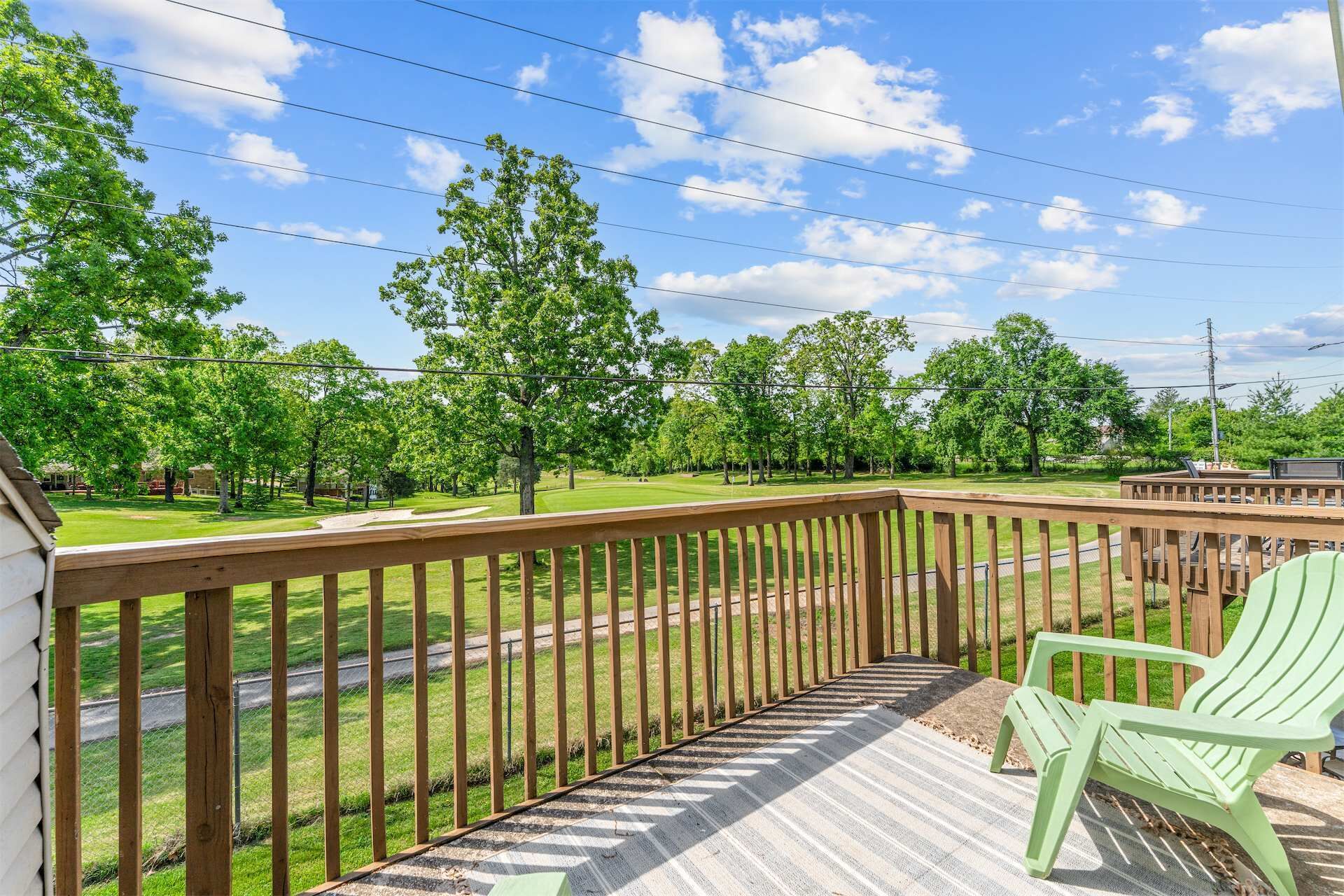 A wooden deck with a railing, a green chair, and a view of a golf course.
