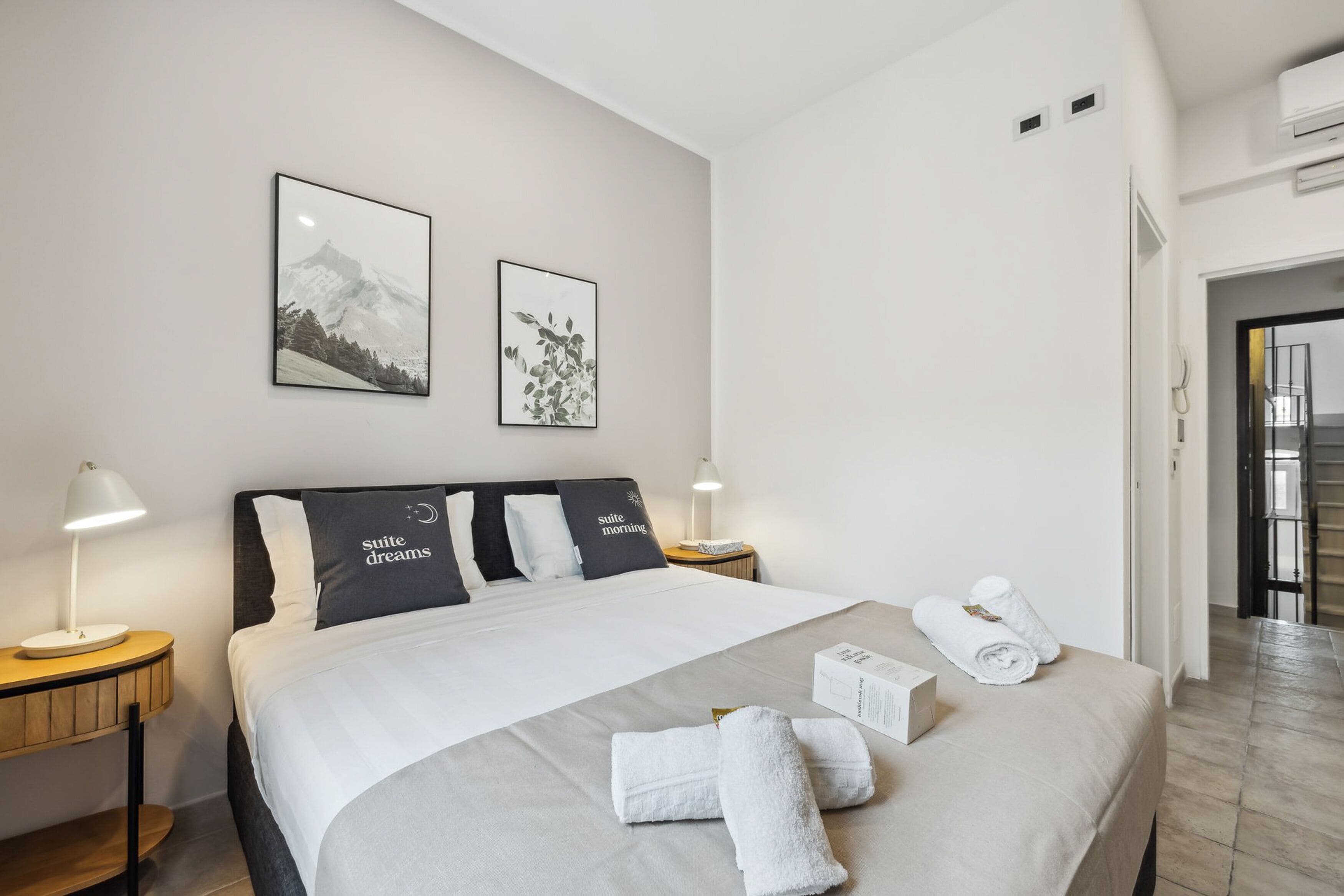 Een hotelkamer met een groot bed, twee nachtkastjes, een deur naar een trap.