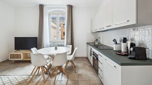 A modern kitchen with white cabinets, a dining table with chairs, and a large window with curtains.