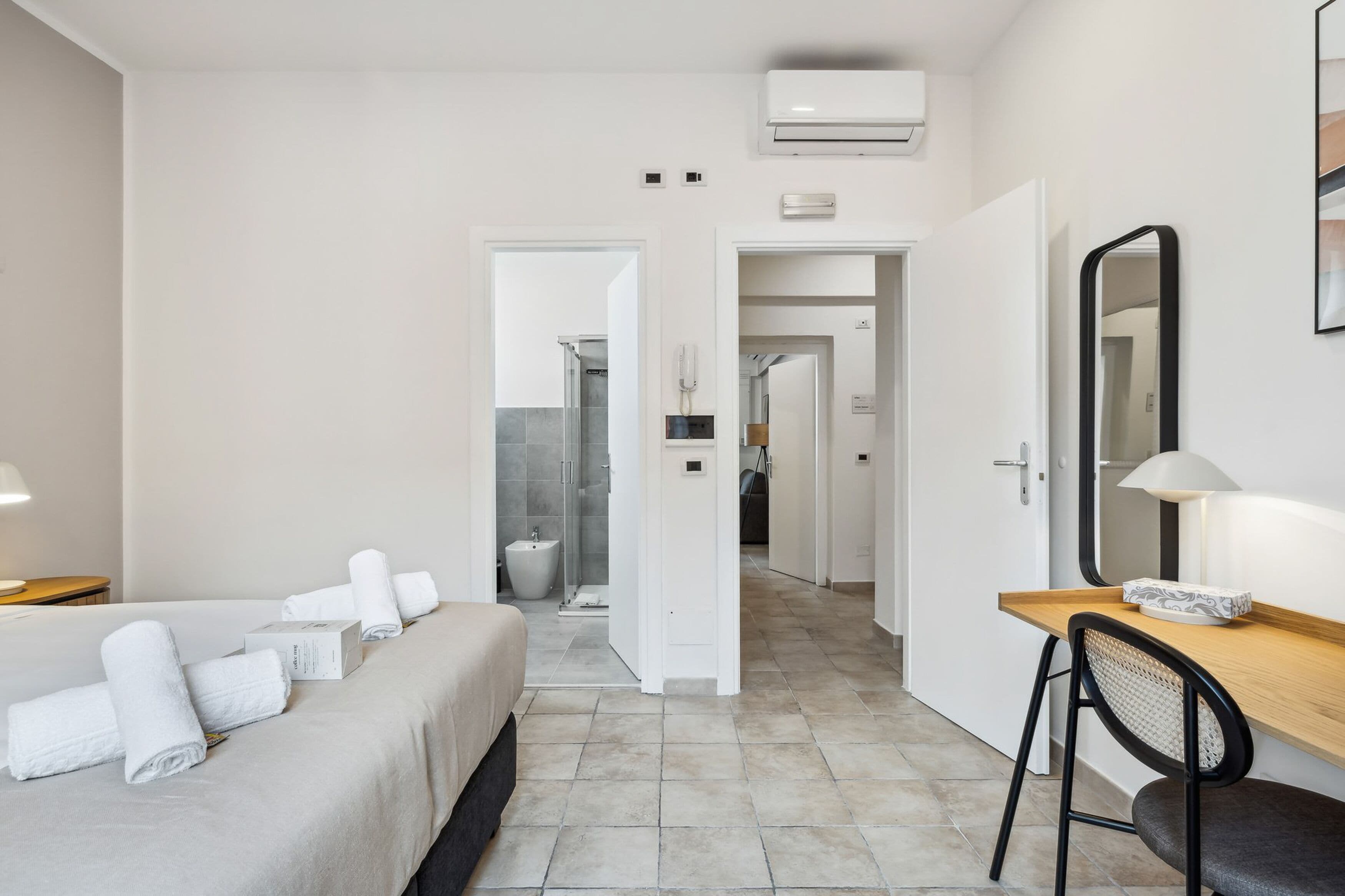 A modern hotel room with a bed, a desk, a chair, and a bathroom visible through an open door.