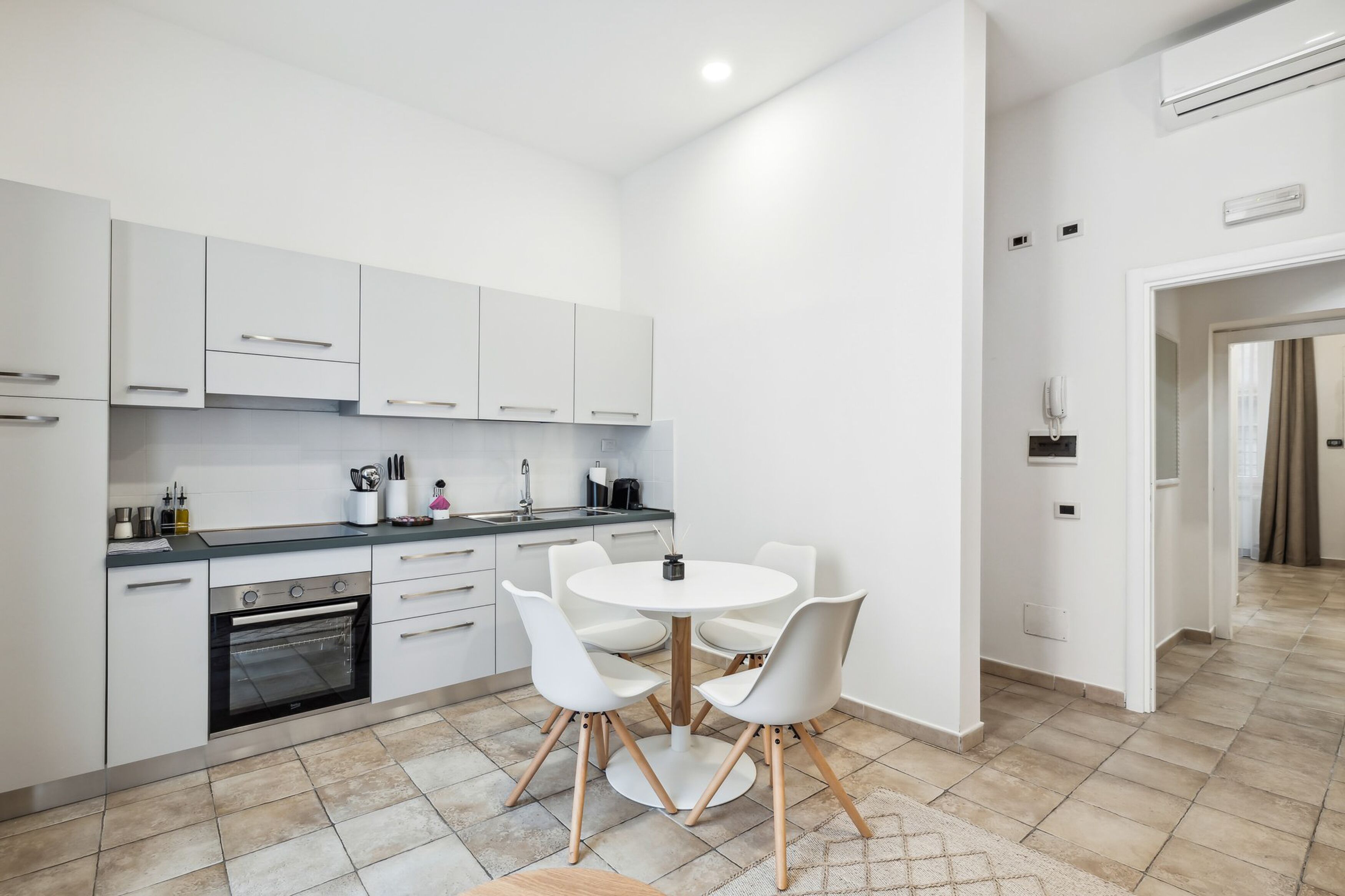 Una cocina moderna con armarios blancos, una mesa redonda de comedor con sillas blancas y un horno empotrado.