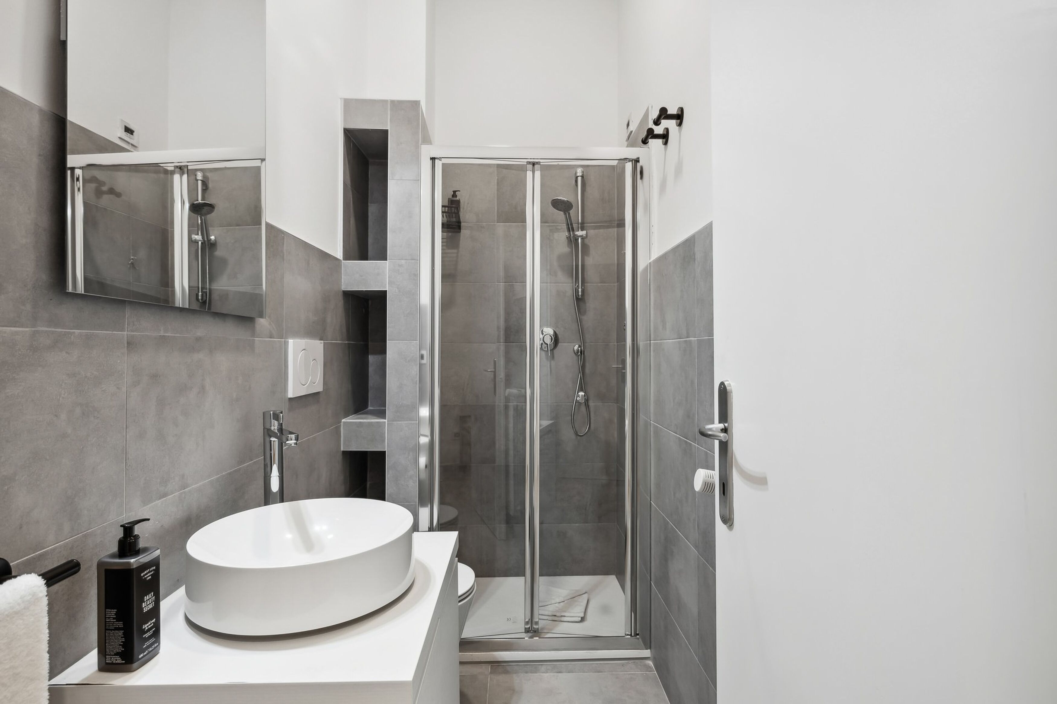 A modern bathroom with a large white sink, a glass-enclosed shower, and a mirror above the sink.