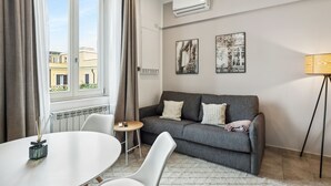 A modern living room with a grey sofa, white chairs, a small round table, and a lamp.