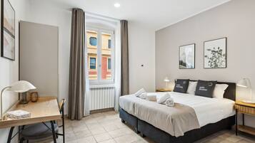 Ein Hotelzimmer mit Bett, Schreibtisch, Stuhl, Fenster mit Vorhängen und Kunstwerken an den Wänden.