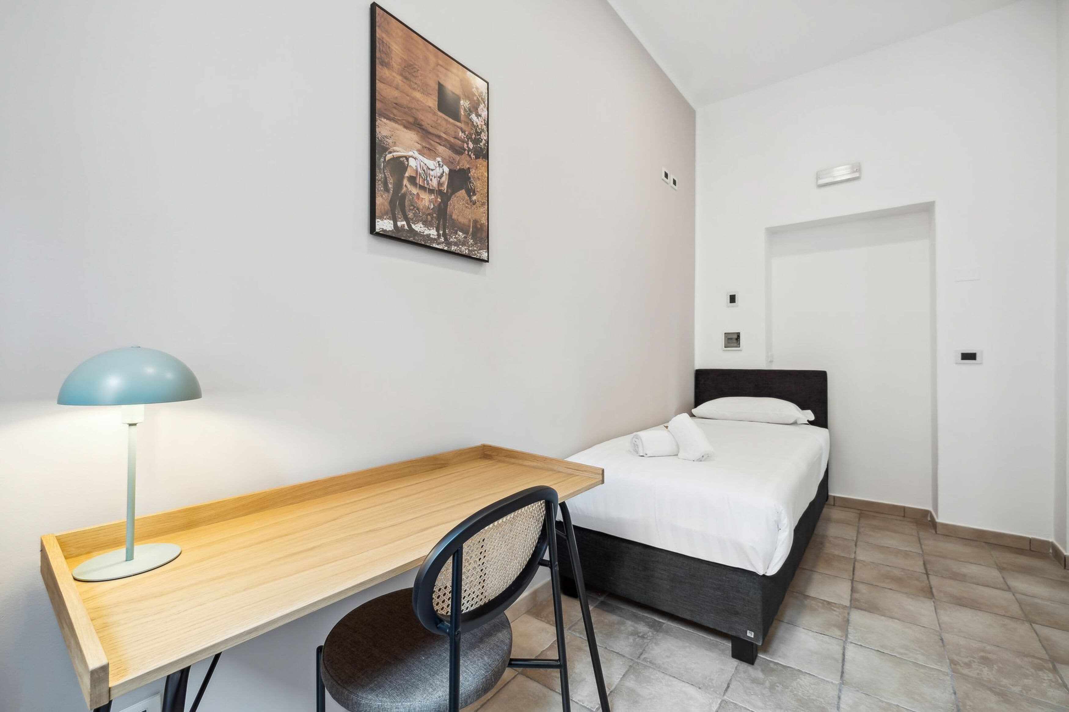 Ein Schlafzimmer mit einem Bett, einem Schreibtisch, einem Stuhl, einer Lampe und einem Bild an der Wand.