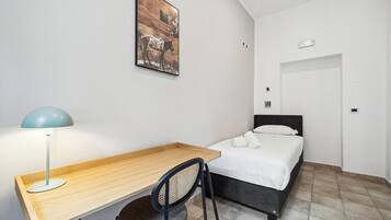 Ein Schlafzimmer mit einem Bett, einem Schreibtisch, einem Stuhl, einer Lampe und einem Bild an der Wand.