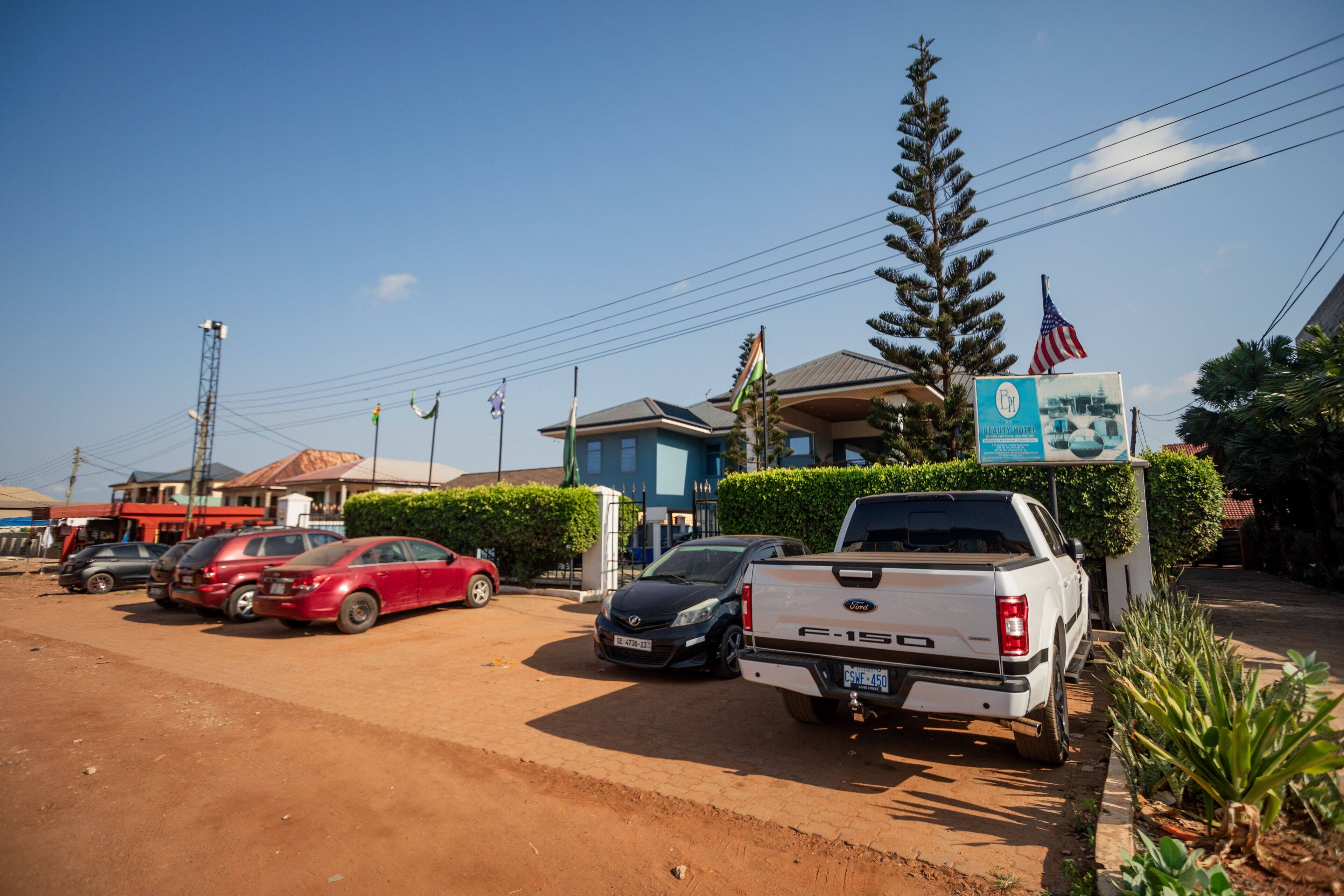 A parking lot with several cars, a white pickup truck, and a building with a blue roof.