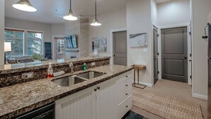 Een moderne keuken met granieten aanrecht, een dubbele spoelbak, hanglampen en uitzicht op de woonkamer.