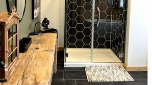 Ein modernes Badezimmer mit einem Holzausziehtisch, einer Duschkabine aus Glas mit Wabermuster und einem dunklen Fliesenboden.