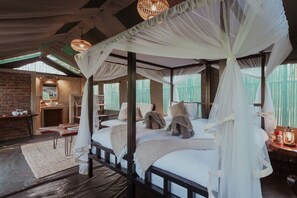 A four-poster canopy bed with white linens and pillows, a rustic brick wall, and a wooden floor. - Sian Simba River Lodge (Victoria Falls)