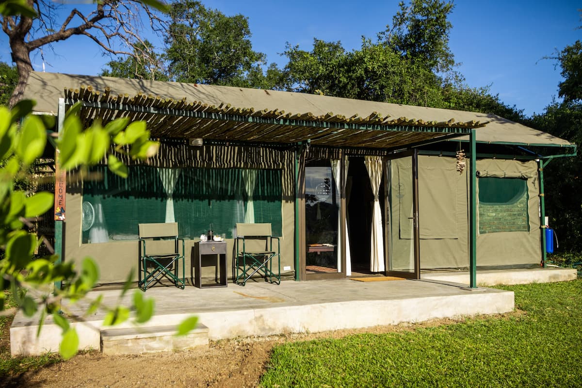 Un espacio al aire libre techado con una mesa y sillas, una mesita adicional y una puerta que da al interior.