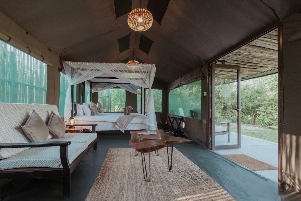 Un dormitorio espacioso con una cama grande, una zona de estar con sofá y mesita de centro, y vistas al exterior a través de amplias ventanas.