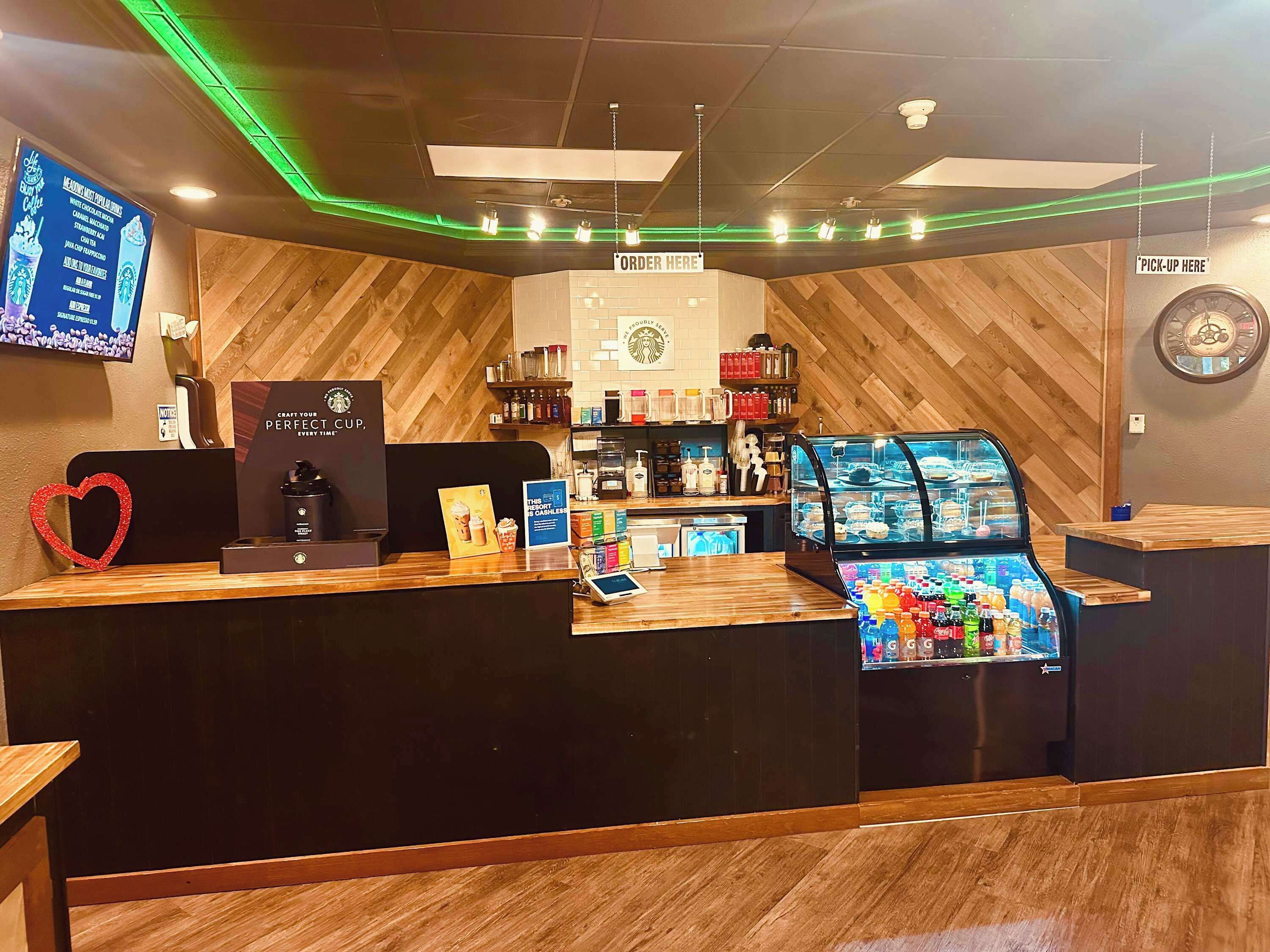 A Starbucks coffee shop interior with a wooden counter, a coffee machine, a display of beverages, and a wall-mounted clock.