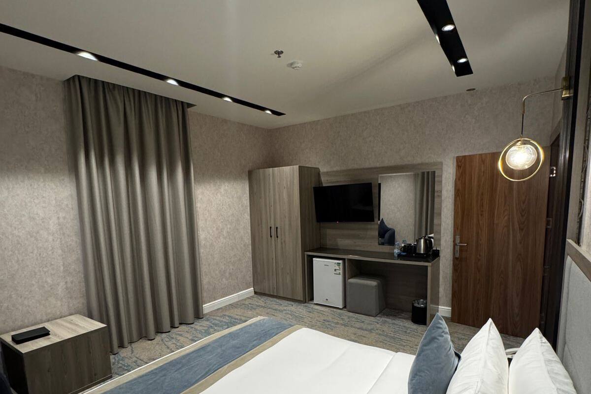 A modern hotel room with a large bed, a desk, a wardrobe, and a kitchenette.