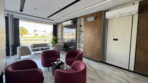 Un intérieur moderne avec un sol en marbre, des fauteuils à revêtement rouge, une table basse en verre et une grande fenêtre donnant sur l’extérieur.