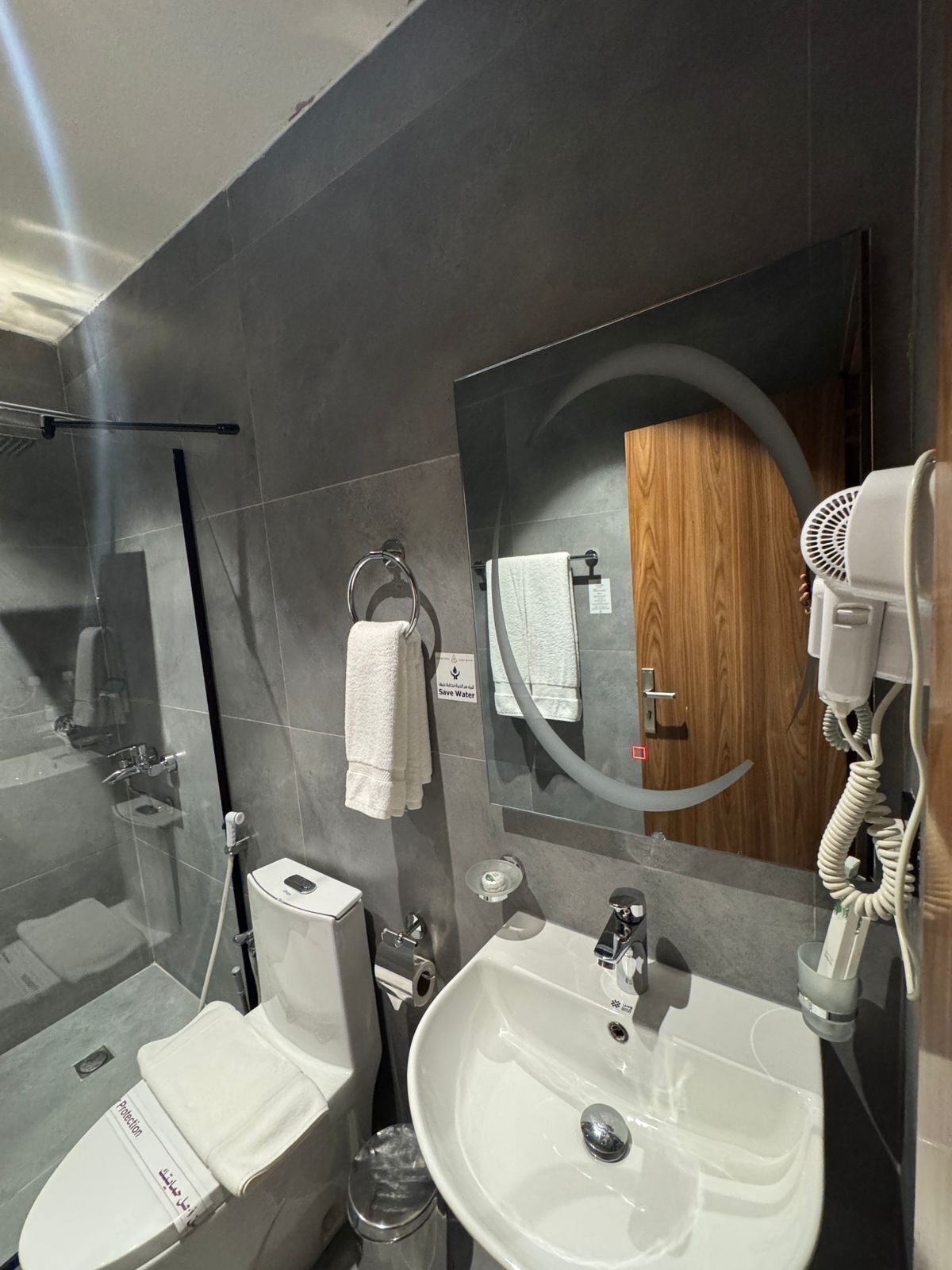 Un baño moderno con un espejo grande, un secador de pelo, un lavamanos y un inodoro.