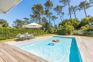 Une piscine rectangulaire dotée d’une terrasse en bois, entourée d’une végétation luxuriante et de grands arbres.