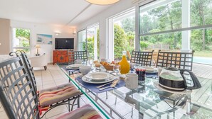 A modern dining area with a glass table, chairs, and a television in the background. - Madame Vacances Villas Club Royal 17 (Moliets-et-Maa)