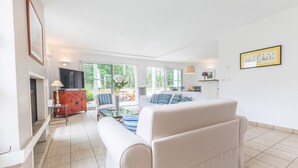 A spacious living room with a sofa, a TV, and a dining area with chairs and a table. - Madame Vacances Villas Club Royal 17 (Moliets-et-Maa)