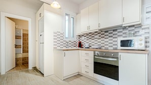 A modern kitchen with white cabinets, a microwave, an oven, and a window. - Alex Home by Corfuescapes (Corfu)
