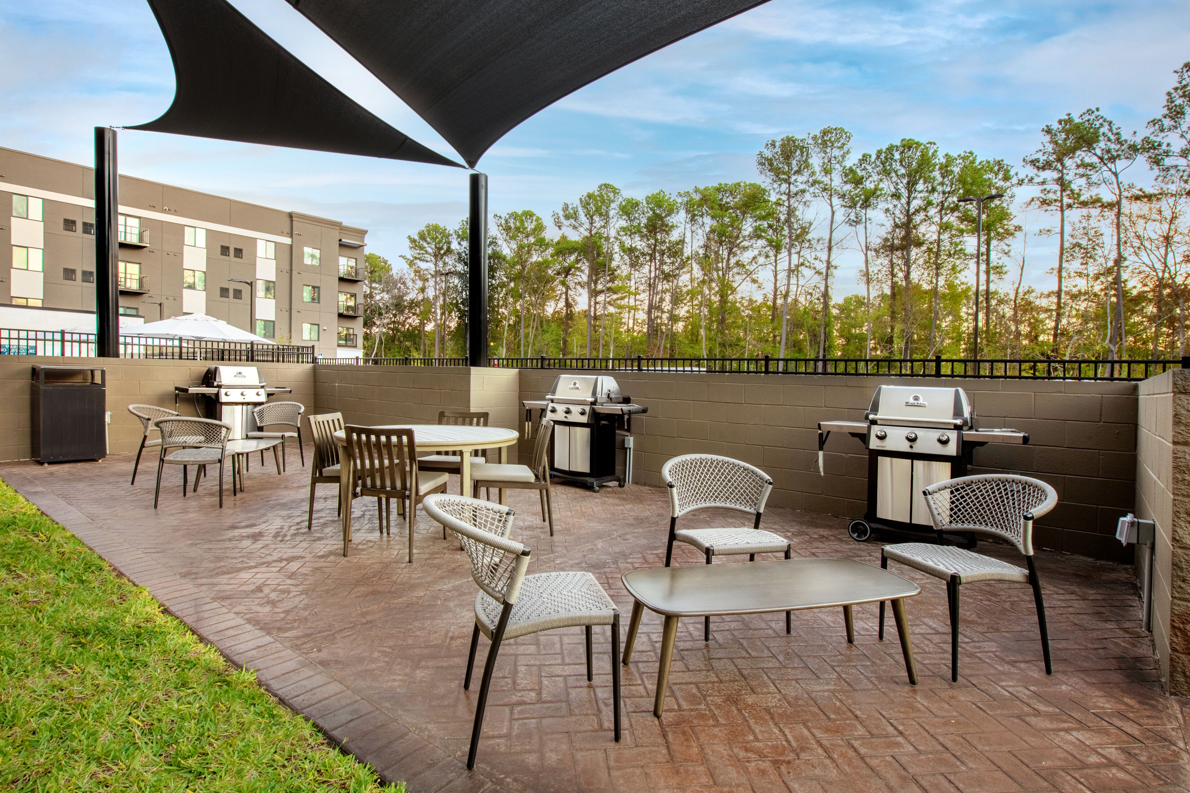 An outdoor patio with a grill, chairs, and tables, surrounded by a brick wall and a fence.
