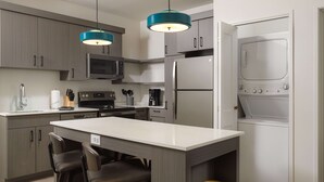 Een moderne keuken met grijze kasten, een centraal eiland met barkrukken, een ingebouwde oven, een magnetron en een roestvrijstalen koelkast.