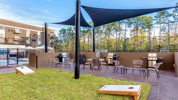 An outdoor patio area with a barbecue grill, seating, and a shaded area.