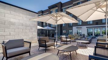 An outdoor patio area with seating arrangements, including sofas and tables, under large umbrellas.