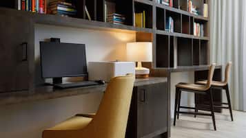 A modern workspace with a desk, computer, and two chairs. A bookshelf filled with books is in the background.