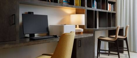 A modern workspace with a desk, computer, and two chairs. A bookshelf filled with books is in the background.