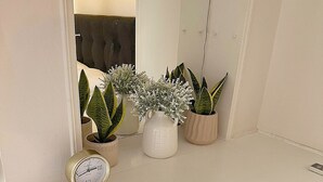 A white dresser with a mirror above it, a small clock, and several potted plants. - Check Point - Parthenon (Athens)