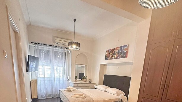 A bedroom with a bed, bedside table, mirror, and a round woven rug. - Check Point - Parthenon (Athens)