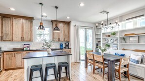 A modern kitchen with wooden cabinets, a central island with stools, pendant lighting, and a dining area with a bench and chairs. - New Property in Carlton Landing-Nolan's Nook- Pet Friendly (Carlton Landing)