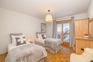 A bedroom with two beds, a wooden wardrobe, a view of mountains, and a hanging light fixture. - Chalet Sapin Argenté (Riddes)