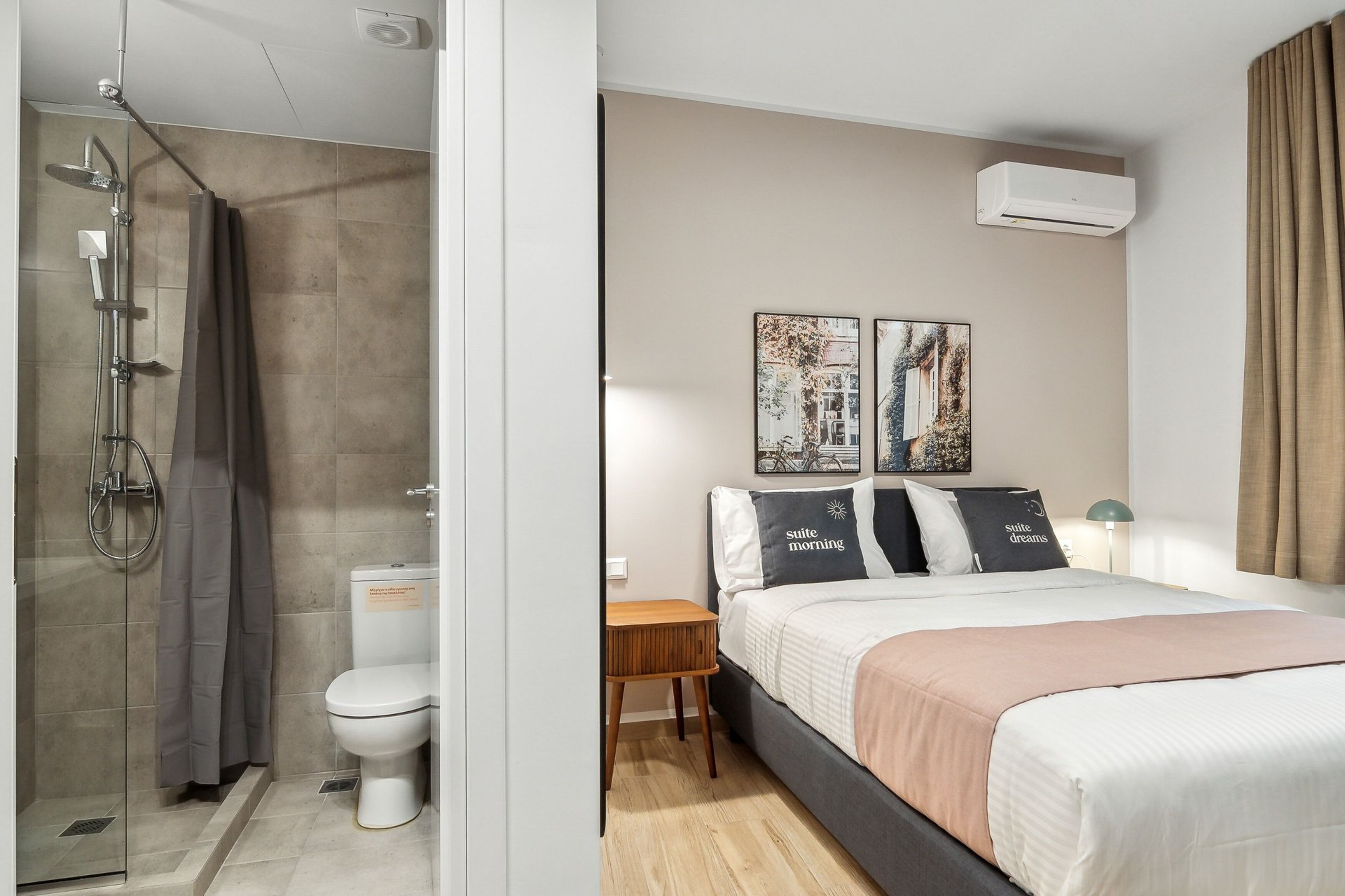 A modern hotel room with a shower, toilet, bed, and artwork on the wall.