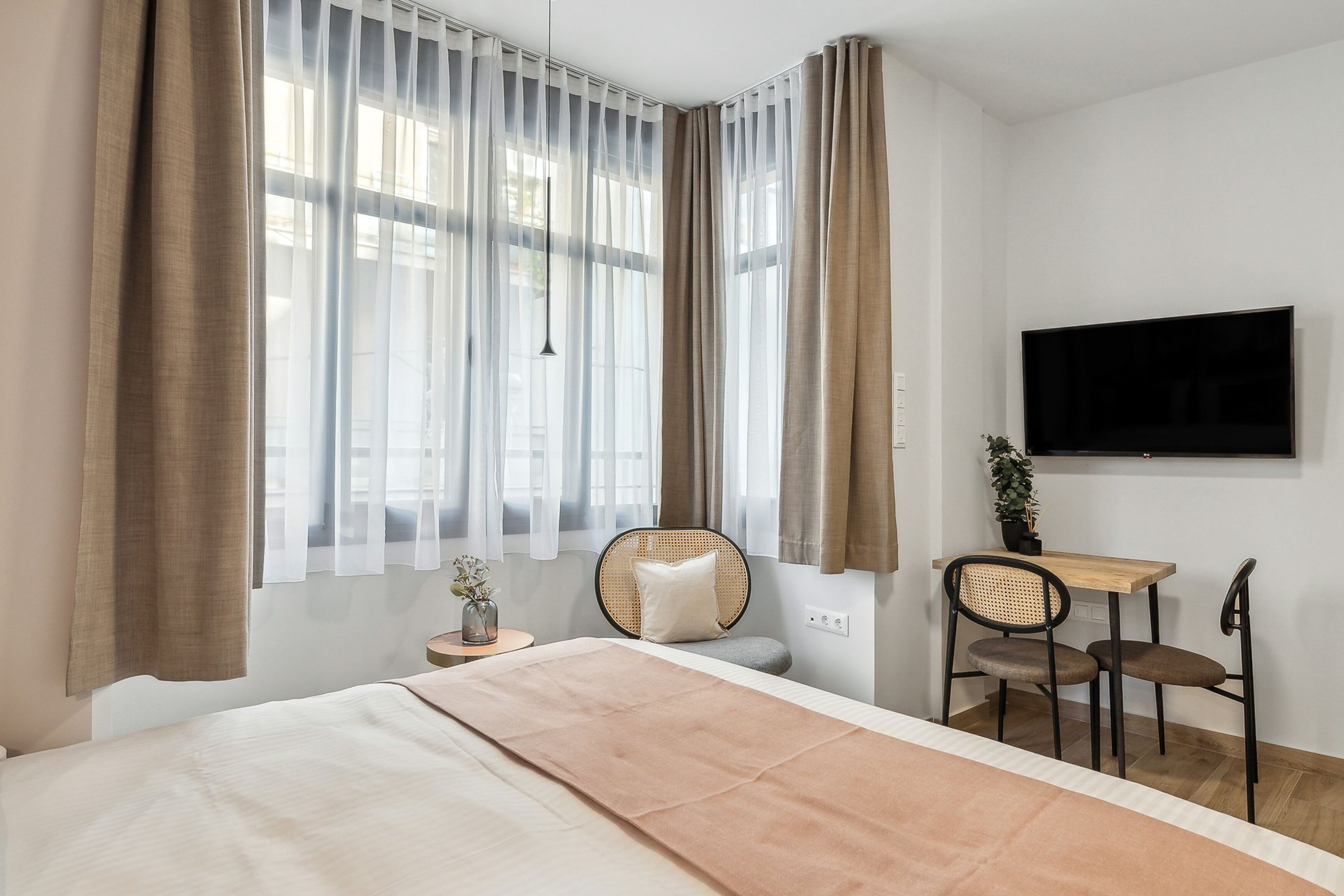 A hotel room with a bed, a desk with two chairs, a TV, and a window with curtains.