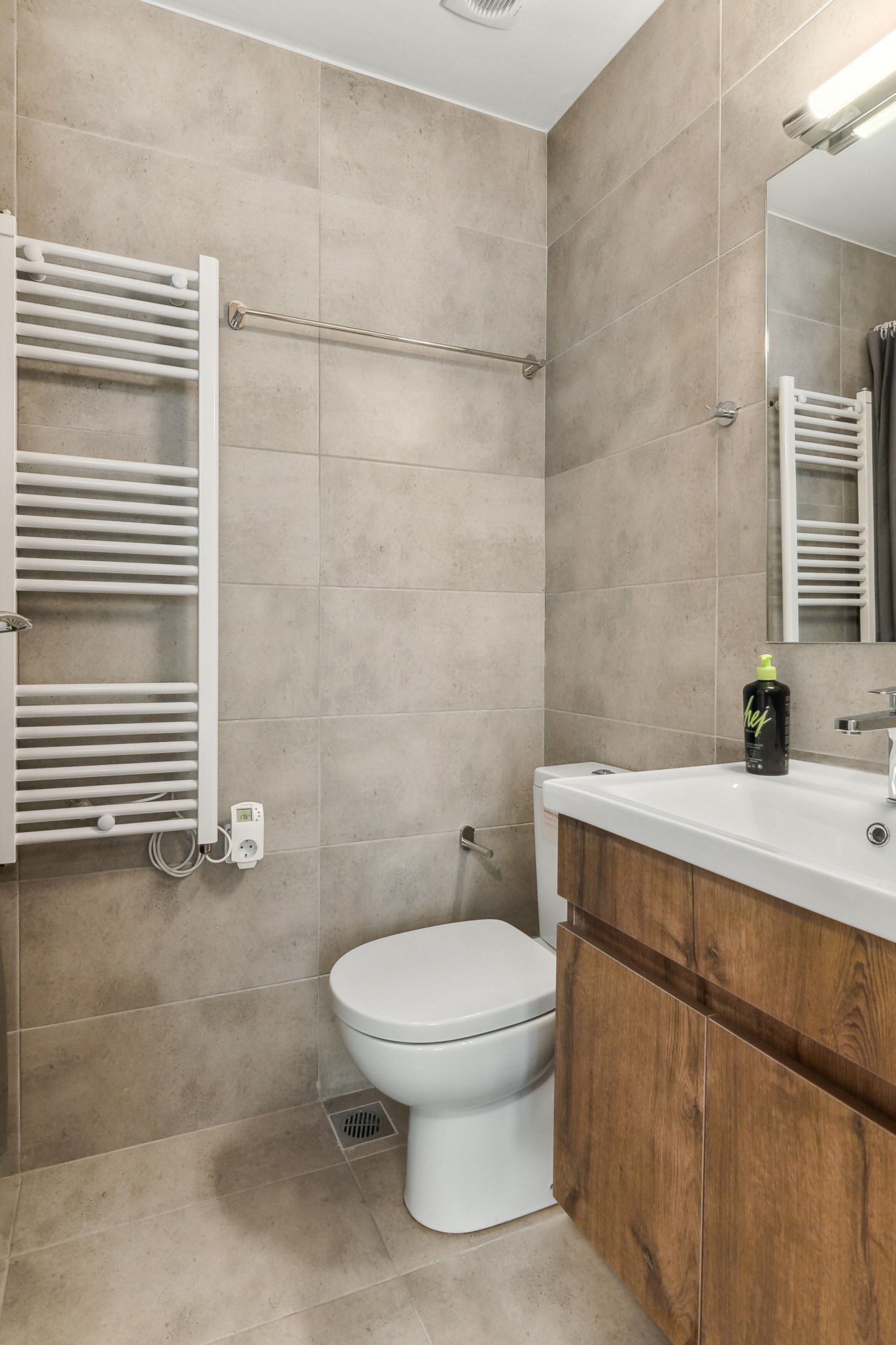 A modern bathroom with a white toilet, beige tiles, a wooden vanity, and a towel rack.
