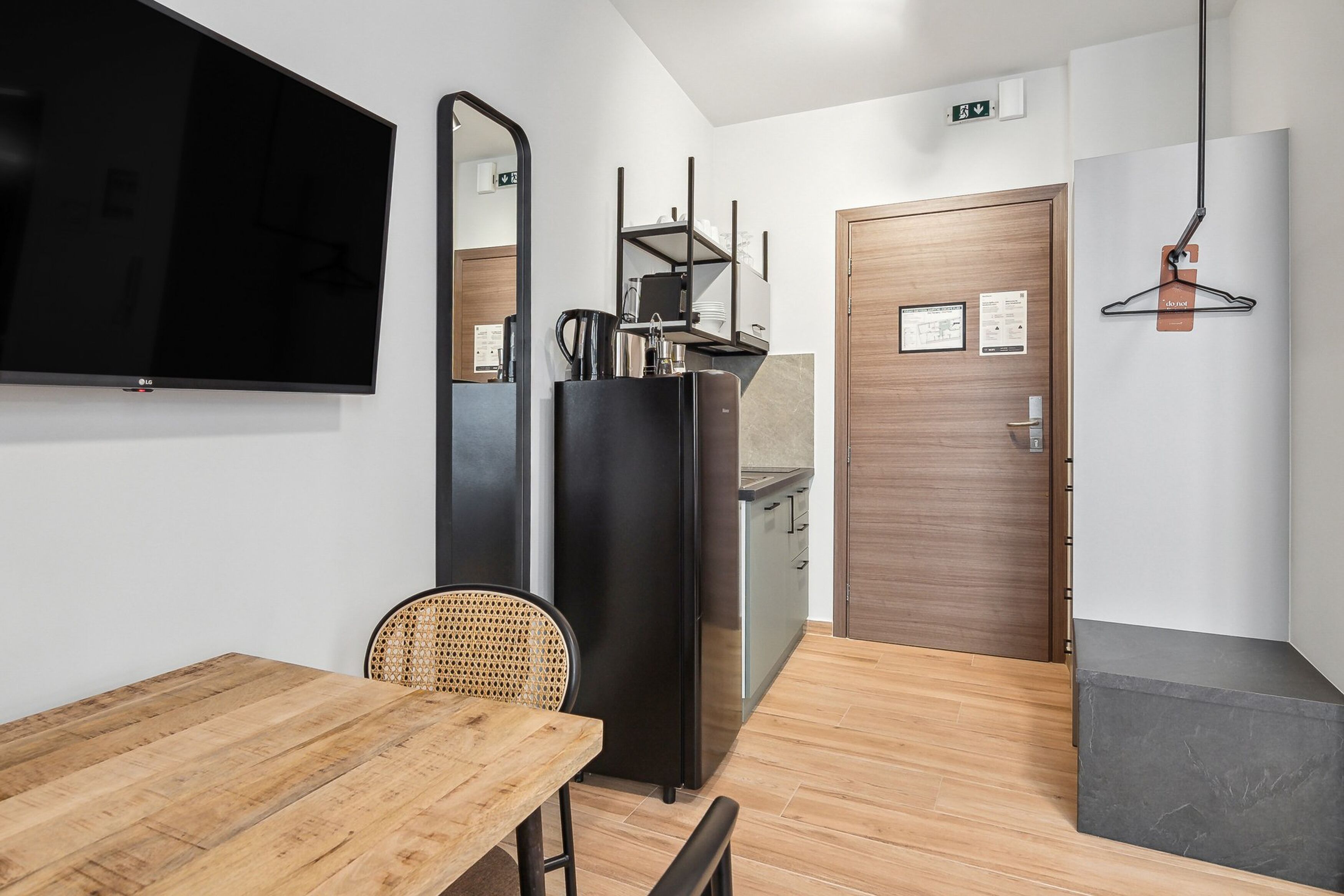 A modern room with a wooden table, a black refrigerator, a flat-screen TV, and a mirror.