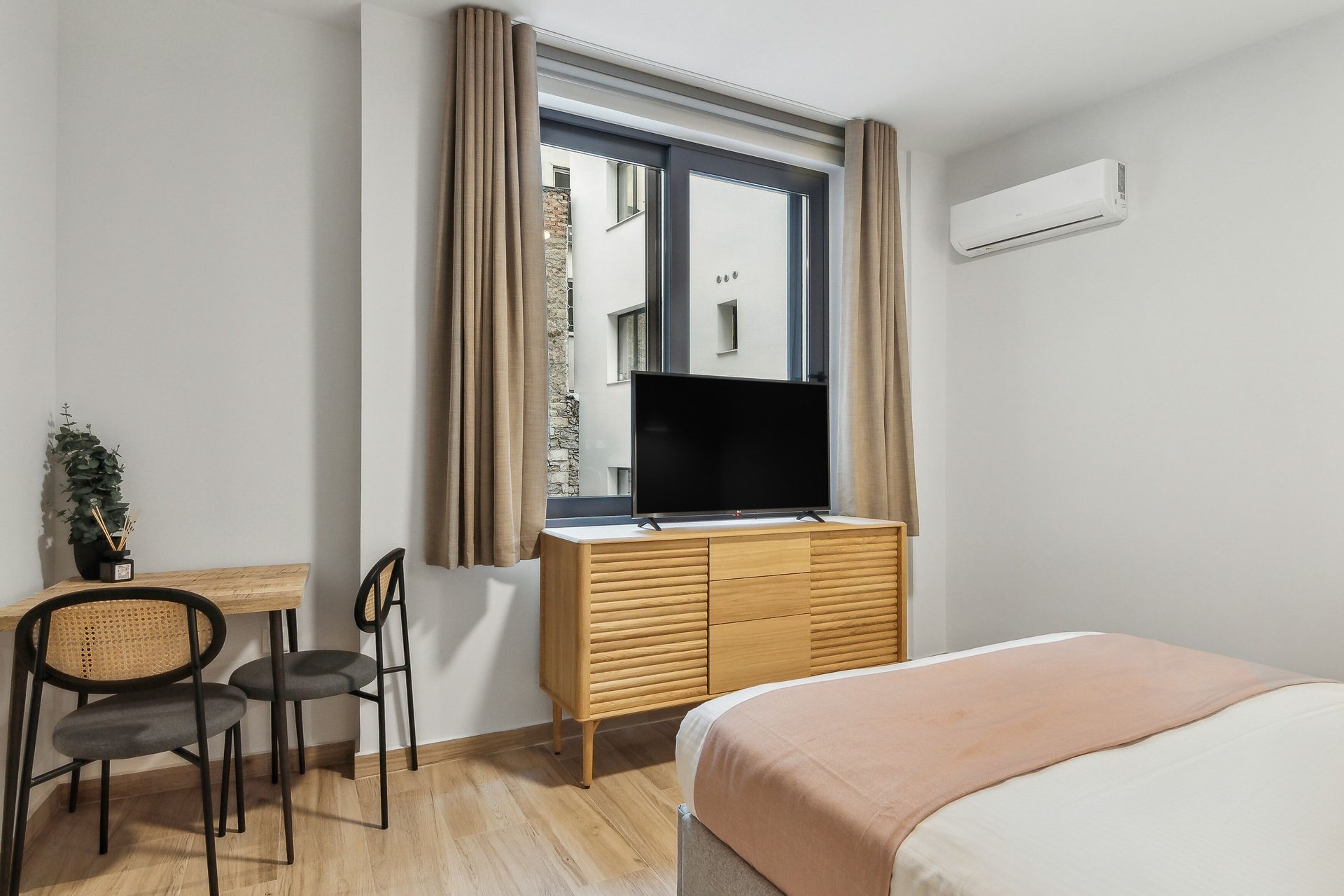 Une chambre d’hôtel comprenant un lit, un bureau avec une télévision, une fenêtre avec des rideaux et un appareil de climatisation.