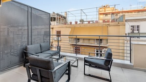 A balcony with a sofa and chairs, a metal railing, and a view of buildings in the background. - Limehome Athens Solonos City Center (Athens)
