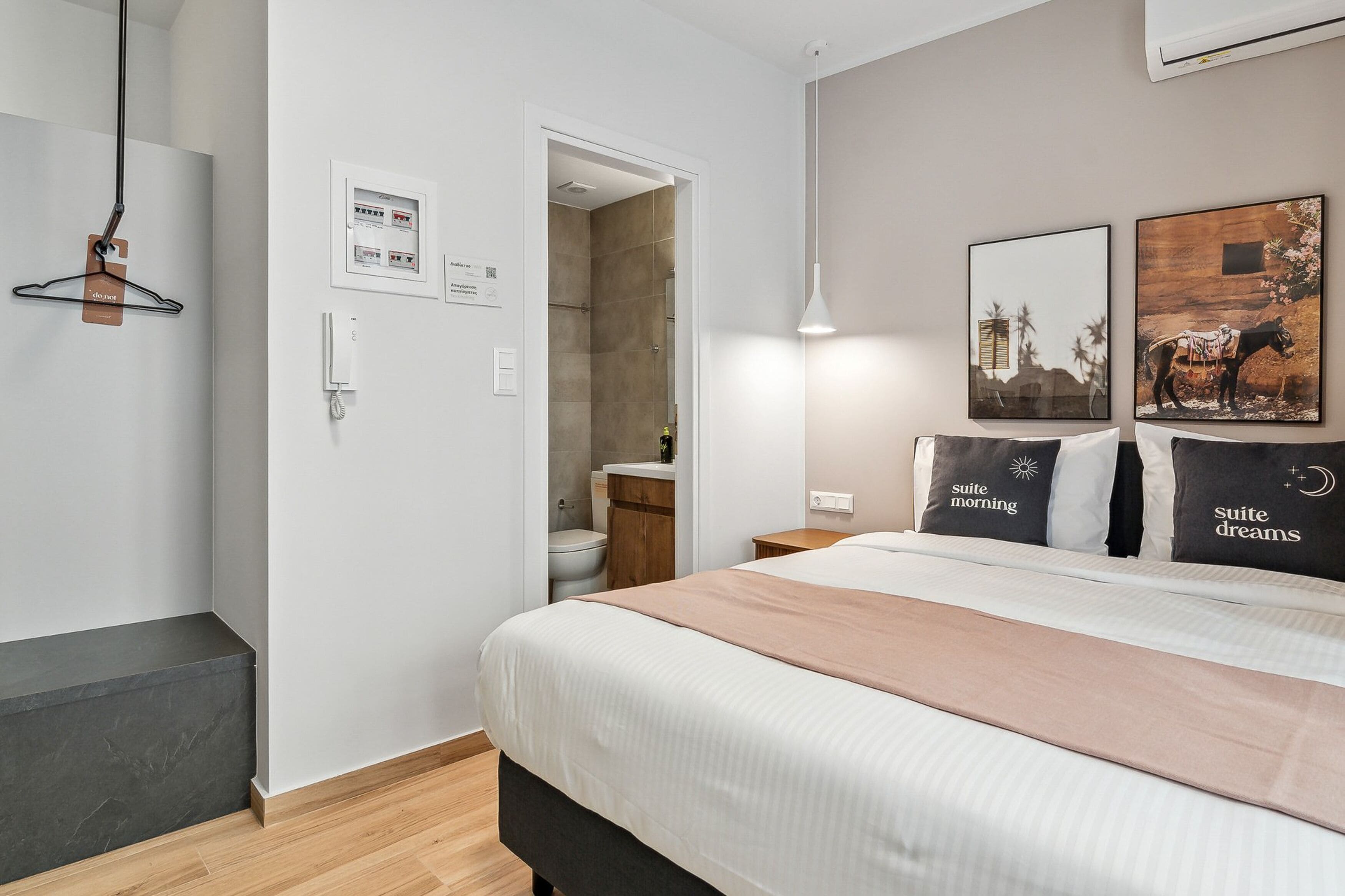 A hotel room with a bed, a bedside table, a hanging light, a shower area, and a wall-mounted air conditioner.
